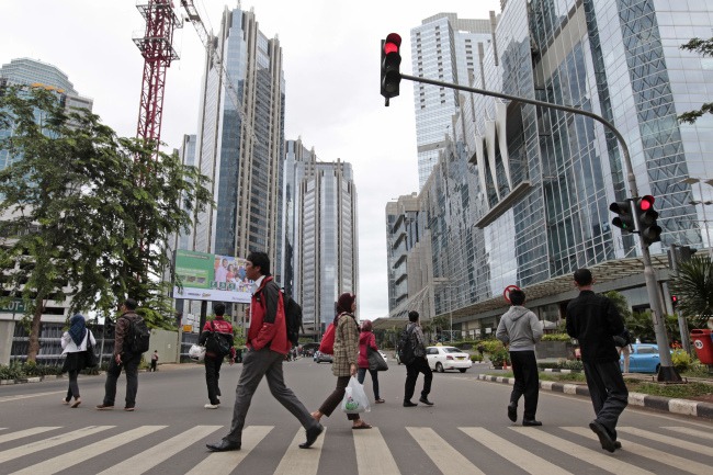 Pedestrians cross a road in front of buildings in the financial district of Jakarta, Indonesia.  Bloomberg