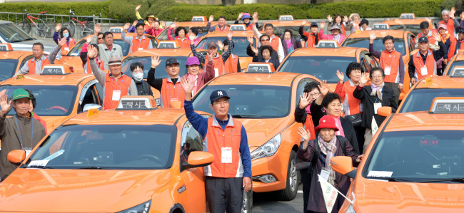 Taxi drivers and senior citizens wave for a photo in the parking lot of Guro-gu Office in Seoul on Tuesday before departing for tourist attractions on Ganghwado Island. The cabbies gave old or disabled people in the district a complimentary ride to tourist sites as a voluntary service.
Kim Myung-sub/The Korea Herald
