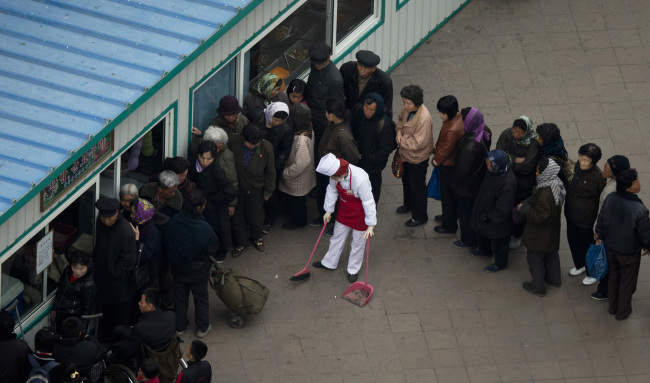 <YONHAP PHOTO-0887> A food shop keeper sweeps with a broom while people line up outside a shop window in Pyongyang, North Korea, Tuesday, April 16, 2013. (AP Photo/Alexander F. Yuan)/2013-04-16 11:45:39/ <저작권자 ⓒ 1980-2013 ㈜연합뉴스. 무단 전재 재배포 금지.>
People line up outside of a food shop in Pyongyang on Tuesday.   AP-Yonhap News