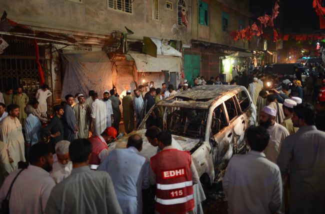 Local residents and volunteers gather around a destroyed vehicle at the site of a suicide bomb attack at an election campaign rally in Peshawar, Pakistan, Tuesday.   AFP-Yonhap News