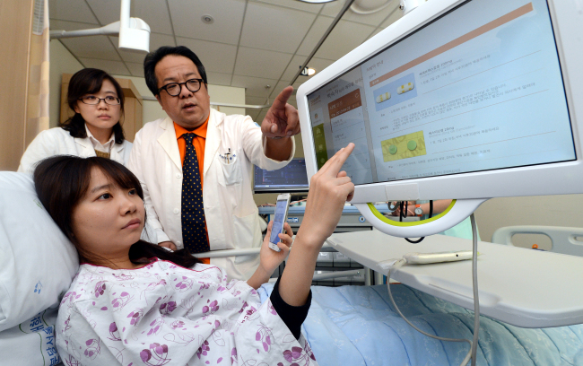 A patient and doctors use an ICT-based “smart hospital solution” program at the Seoul National University Bundang Hospital in Gyeonggi Province on Monday. Health Connect, a joint venture between SK Telecom and Seoul National University Hospital, commercialized the solution system which provides patients or visitors with various services such as submitting applications for medical checkups and paying hospital bills through digital devices.   Ahn Hoon/The Korea Herald
