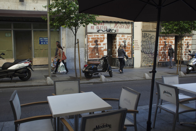 Pedestrians pass closed-down stores opposite an empty cafe terrace in Madrid.   Bloomberg