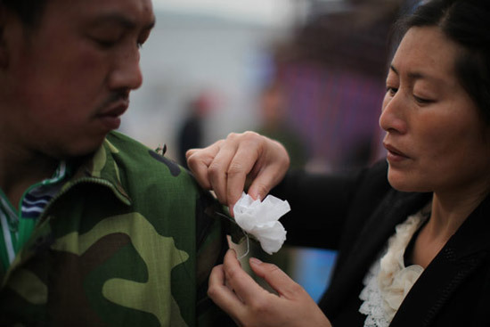 A woman pins a paper flower on her husband’s sleeve on Saturday in Renjia village, Qingren township, in Sichuan province’s Lushan county, to pay respect to those who died in the earthquake.   China Dailya