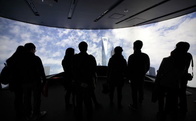 Visitors look at a monitor displaying an image of the Shanghai World Financial Center in the Pudong area of Shanghai.    Bloomberg
