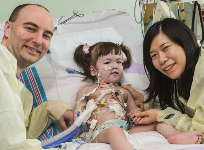 Darryl Warren and Lee Young-mi visit with their 2-year-old daughter Hannah Warren in a post-op room at Children’s Hospital of Illinois in Peoria after having received a new windpipe in a landmark transplant operation April 9. Hannah was born in South Korea without a windpipe but received a new one made from her own stem cells.   AP-Yonhap News