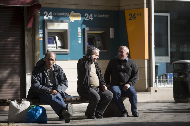 Men sit near 24-hour automated teller machines operated by Bank of Cyprus in Nicosia, Cyprus.   Bloomberg