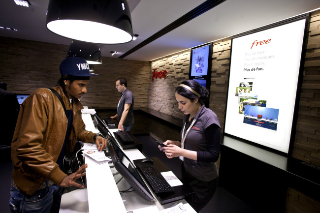 A employee (right) serves a customer at the service counter in a “Free Center” mobile store, operated by the Free mobile phone service and owned by Iliad in Paris.   Bloomberg