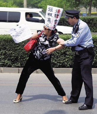A Chinese police officer tries to restrain a petitioner protesting against corruption and injustice on a road near a hotel in Beijing. (AP-Yonhap News)