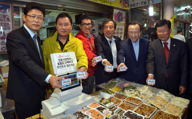 SK Telecom executive vice president Lee Hyung-hee (left) and Incheon Sinki Market merchant association chief Kim Jong-rin (second from left), along with city officials and politicians, trial an IT solution program that the mobile carrier is providing to traditional markets to help their competitiveness on Monday.   Kim Myung-sub/The Korea Herald