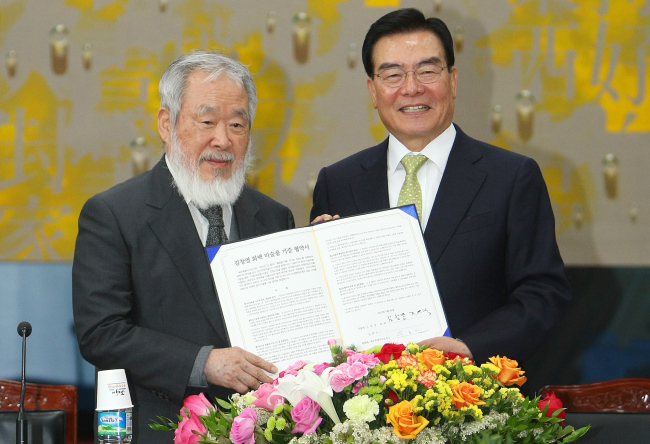 Artist Kim Chang-yeol (left) poses in front of photographers with Jeju Gov. Woo Keun-min at an agreement signing ceremony at a Jeju Special Self-Governing Province office on Monday.   Yonhap News