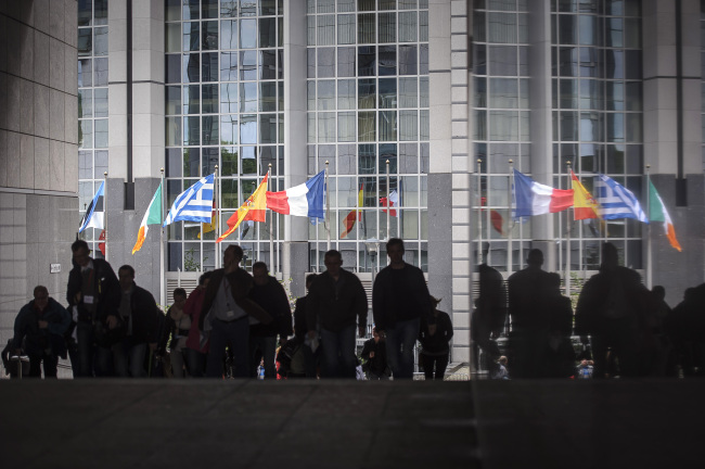 Pedestrians walk past the European Union parliament building and the national flags of the member states in Brussels.   Bloomberg