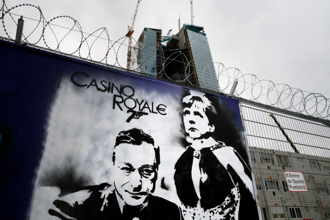Graffiti depicting ECB president Mario Draghi and Chancellor Angela Merkel sits on boards outside the construction site of the European Central Bank's (ECB) new headquarters in Frankfurt, Germany, on Wednesday, May 22, 2013. European leaders decided in June last year to hand powers to oversee European banks to the Frankfurt-based ECB, as part of a so-called banking union to break the link between governments' creditworthiness and commercial lenders. Photographer: Ralph Orlowski/Bloomberg
Graffiti depicting ECB president Mario Draghi and German Chancellor Angela Merkel is shown on boards outside the construction site of the European Central Bank’s new headquarters in Frankfurt on Wednesday.   Bloomberg