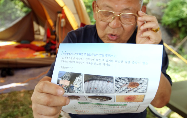 <YONHAP PHOTO-0830> '야생 진드기' 안내장 보는 제주 야영객 (서귀포=연합뉴스) 고성식 기자 = 제주도 서귀포시 성산읍 모구리 야영장을 찾은 야영객들이 24일 제주도로부터 받은 '야외 활동 시 야생 진드기 주의사항'을 담은 안내장을 차근히 읽어보고 있다. 제주도는 올레길과 야영장 등을 찾는 관광객과 도민에게 안내장을 나눠주고 통행로 주변에 안내문을 설치해 주의를 당부하기로 했다. 2013.5.24 koss@yna.co.kr/2013-05-24 14:41:35/ <저작권자 ⓒ 1980-2013 ㈜연합뉴스. 무단 전재 재배포 금지.>
A camper in Jeju reads a guideline for tick-borne virus prevention Friday.   Yonhap News