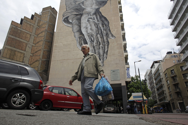A man carries his shopping bags past a giant wall mural in Athens.   Bloomberg