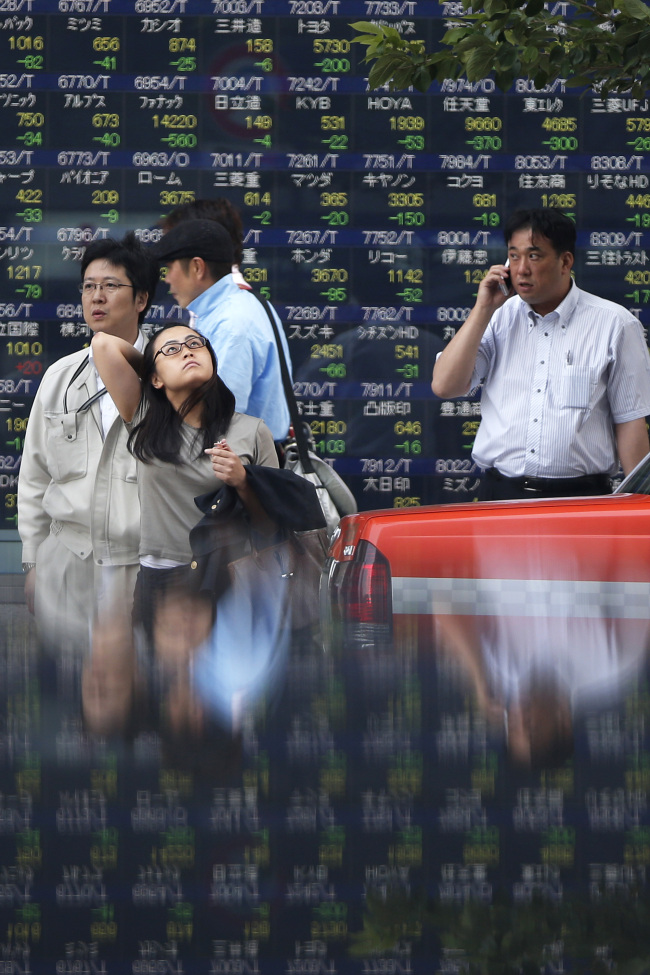 Pedestrians wait to cross a road in front of an electronic stock board outside a securities firm in Tokyo on Wednesday.   Bloomberg
