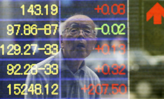 A man is reflected on the electronic board of a securities firm in Tokyo on Monday.   AP-Yonhap News