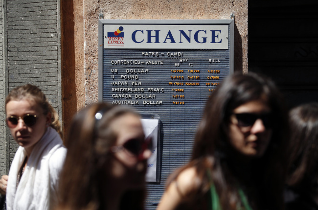 Pedestrians pass a board displaying foreign exchange rates in Rome.   Bloomberg