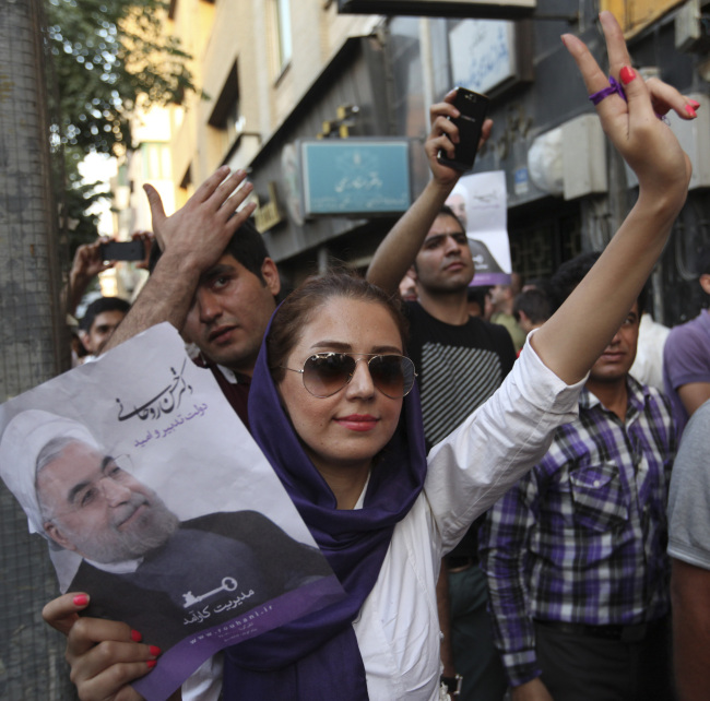 A female supporter of Iranian presidential candidate Hasan Rowhani flashes a victory sign, as she holds his poster, during a celebration gathering, in Tehran, Saturday.   AP-Yonhap News