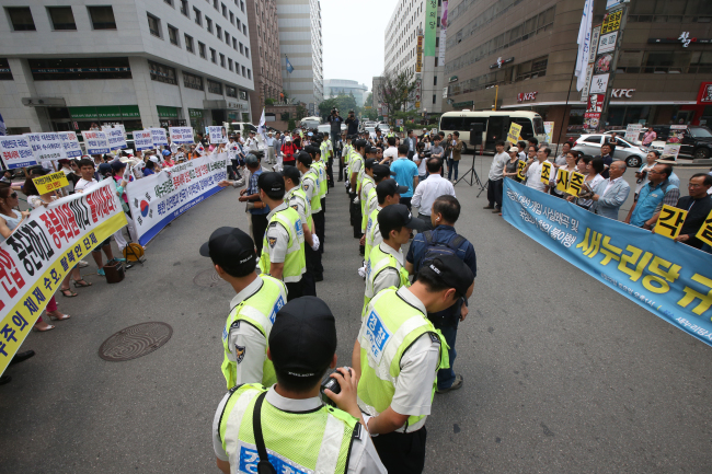 <YONHAP PHOTO-0588> 경찰 사이에 두고 (서울=연합뉴스) 서명곤 기자 = 22일 오후 여의도 새누리당사 앞에서 진보단체가 '국정원 대선 개입 사실왜곡 및 국정조사 합의 불이행 새누리당 규탄대회'(오른쪽)를 열자 애국주의 연대 등 보수단체가 집회신고 없이 '맞불' 집회를 열고 있다. 2013.6.22 seephoto@yna.co.kr/2013-06-22 14:44:47/ <저작권자 ⓒ 1980-2013 ㈜연합뉴스. 무단 전재 재배포 금지.>
A line of police officers divide members of progressive non-governmental organizations (right) and members of conservative NGOs as they stage protests outside the Saenuri Party’s headquarters in Yeouido, Seoul on Saturday. Yonhap News