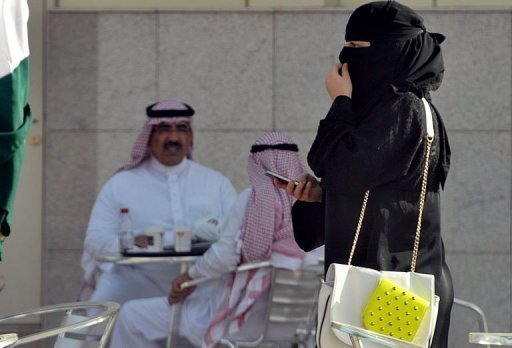 A woman holds her cellphone as she walks past a coffee shop in the Saudi capital Riyadh.   AFP-Yonhap News