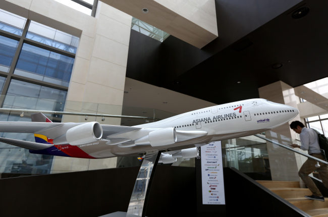 A man using a mobile phone walks past an Asiana Airlines Inc. model aircraft displayed at the company’s headquarters in Seoul.   Bloomberg