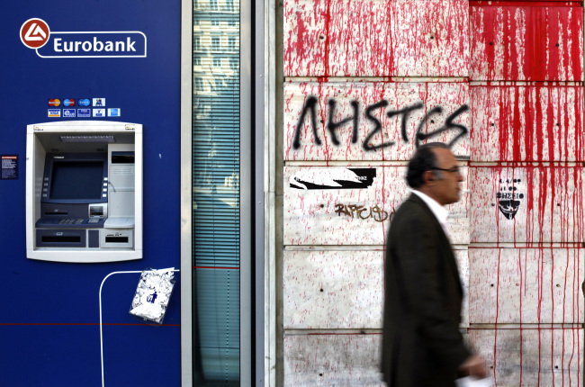 A pedestrian passes a wall covered in graffiti next to the Eurobank in Athens.    Bloomberg