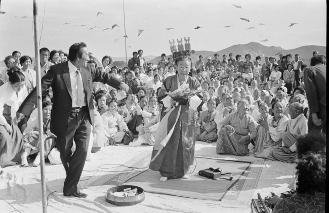 A shaman in her costume performs a ritual to show respect to the king of the sea at a seaside village in Tongyeong, South Gyeongsang Province, in the 1980s.   The National Folk Museum of Korea