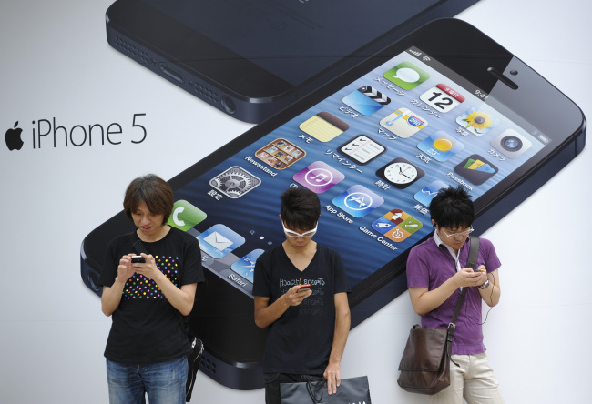 People stand outside a store advertising the iPhone 5 in Tokyo.    Bloomberg
