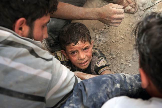 Syrian volunteers try to evacuate 10-year-old Mahmud Fayad still trapped under the rubble of a destroyed house after a barrel bomb was dropped from an air force helicopter in Saraqeb in northwestern Syria on Tuesday.   AFP-Yonhap News