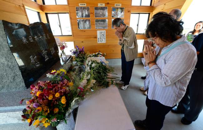 In this picture taken on July 20, tourists pray for victims in front of a monument built in a devastated area in Rikuzentakata, Iwate prefecture.   AFP-Yonhap News