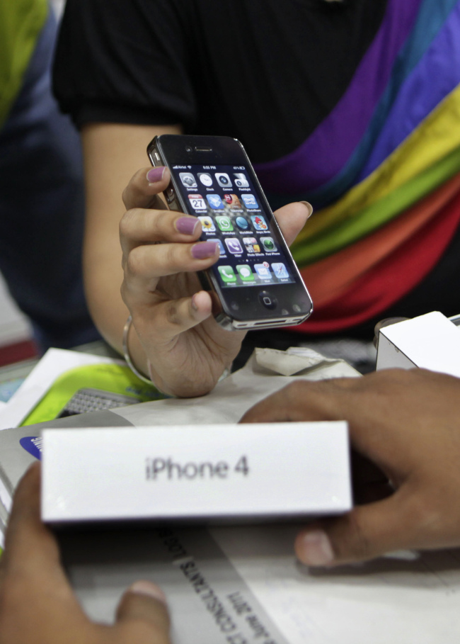 A salesperson at a mobile phone shop displays an Apple iPhone 4 to a customer in New Delhi.   AP-Yonhap News
