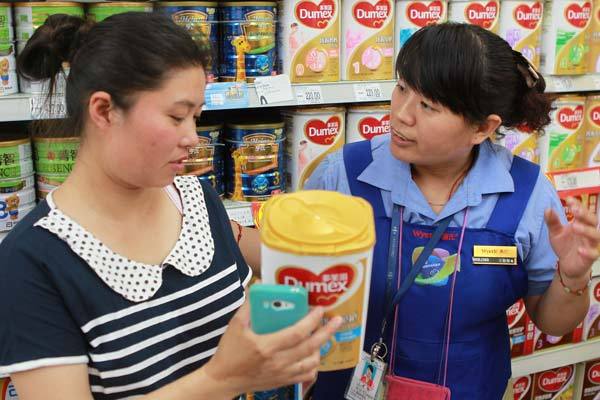 Mu Liping (left) checks with a saleswoman at a supermarket in Beijing on whether her newly bought Dumex baby formula should be recalled.   China Daily