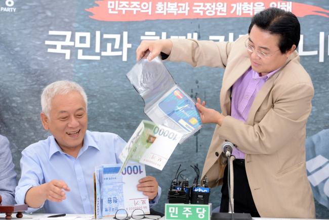 Jun Bung-hun (right), Democratic Party floor leader, shows a transparent envelope highlighting the possible tax burden increase on salaried people under the new government policy. At his side is chairman Kim Han-gil. (Ahn Hoon/The Korea Herald)