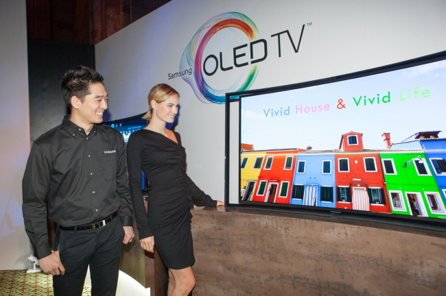 Models pose with Samsung Electronics’ first 55-inch curved OLED TV with full HD capabilities at a launch in New York on Tuesday.   Samsung Electronics