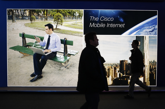 Visitors pass an illuminated Cisco Systems Inc. advertisement at the Mobile World Congress in Barcelona.   Bloomberg