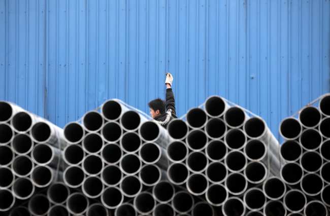 A worker stands behind stacked steel pipes at a storage yard in Shanghai.  Bloomberg
