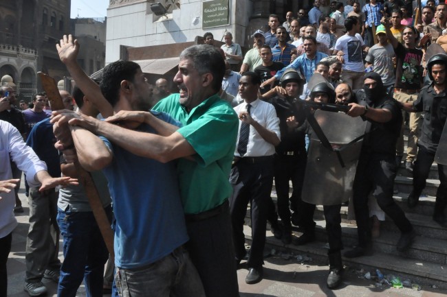 Egyptian security forces escort an Islamist supporter of the Muslim Brotherhood out of the al-Fatah mosque and through angry crowds, after hundreds of Islamist protesters barricaded themselves inside the mosque overnight, following a day of fierce street battles that left scores of people dead, near Ramses Square in downtown Cairo on Saturday.   AP-Yonhap News