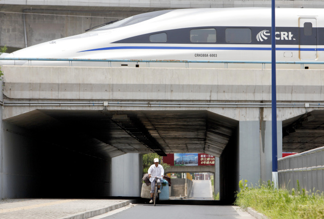 A man cycles through a tunnel under a parked high-speed bullet train at a rail maintenance center in the outskirts of Shanghai.    Bloomberg