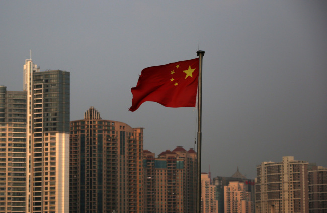 A Chinese national flag flies in front of residential buildings in the Lujiazui district of Shanghai.   Bloomberg