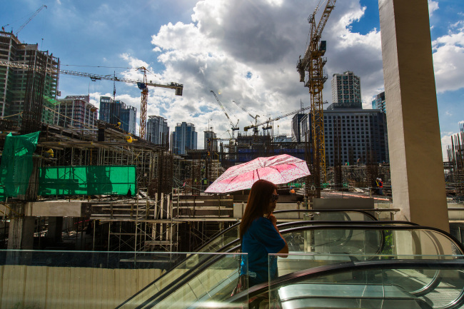 A woman carrying an umbrella rides an escalator past a construction site in the Fort Bonifacio district of Manila.   Bloomberg
A woman carrying an umbrella rides an escalator past a construction site in the Fort Bonifacio district of Manila.   Bloomberg