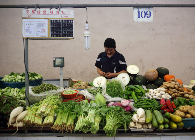 A vendor stands at a vegetable stall at a market in Shanghai.   Bloomberg