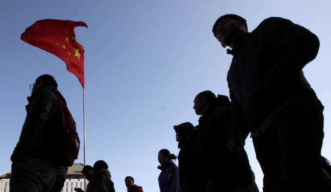 Shoppers and pedestrians walk past a Chinese national flag displayed outside a department store in Beijing.    Bloomberg
