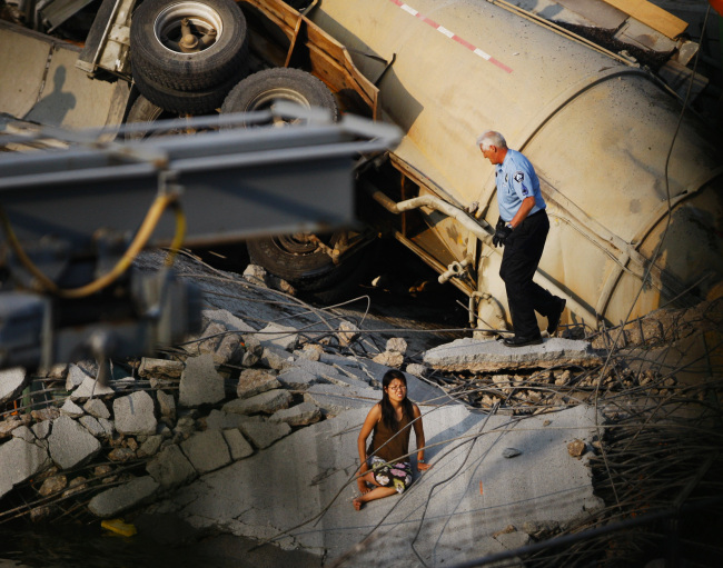 In this Aug. 1, 2007 file photo, a police officer approaches a woman sitting on the collapsed deck of the I-35W bridge in Minneapolis.   AP-Yonhap News