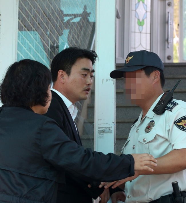 United Progressive Party spokesman Hong Sung-kyu (center) talks with a policeman as National Intelligence Service investigators raid his residence in Hwaseong, Gyeonggi Province, Tuesday in connection with allegations that party members plotted an armed rebellion. (Yonhap News)