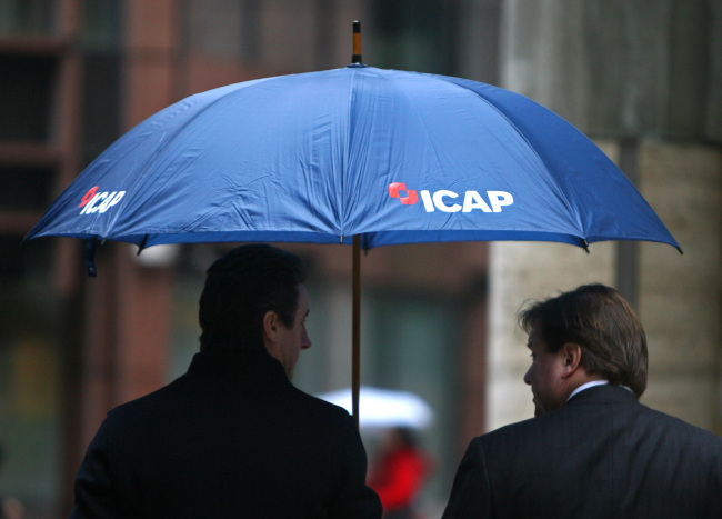 Two men shelter under an umbrella bearing the ICAP logo in London.   Bloomberg