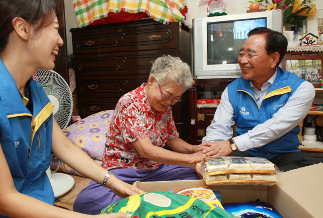 Shinhan Financial Group chairman Han Dong-woo (right) encourages an economically underprivileged elderly woman at her residence in Jongno, Seoul, Sept. 10.   Shinhan Financial Group