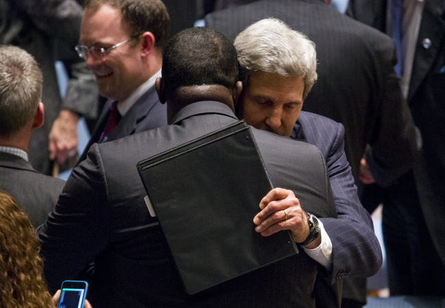 U.S. Secretary of State John Kerry embraces Rwanda’s Ambassador Eugene-Richard Gasana after a session where the United Nations Security Council, meeting on the situation in Syria, voted on a resolution that will require Syria to give up its chemical weapons at U.N. headquarters on Friday.   (AP-Yonhap News)