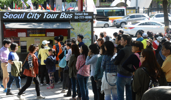 Foreign tourists queue up to take a Seoul City tour bus in Gwanghwamun on Thursday.   (Chung Hee-cho/The Korea Herald)