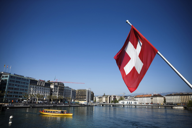 A Swiss national flag flies from a flagpole above Lake Geneva.   Bloomberg