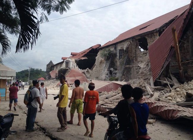 People walk past the damaged Church of San Pedro in Bohol, Philippines, after a magnitude-7.2 earthquake struck the region on Tuesday.   AFP-Yonhap News